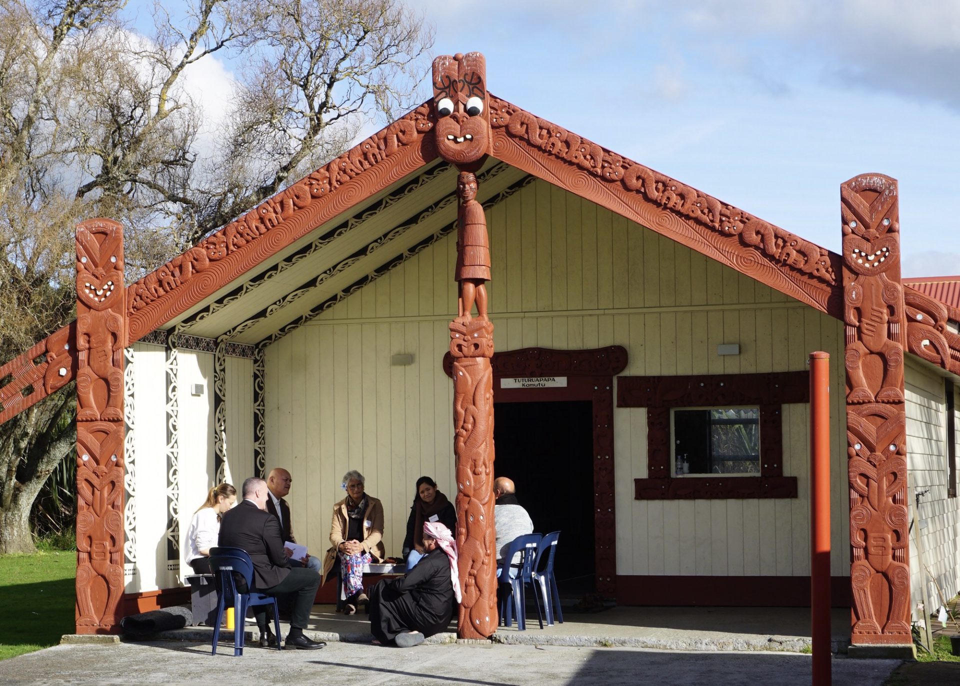 Group sitting in front of marae in discussion